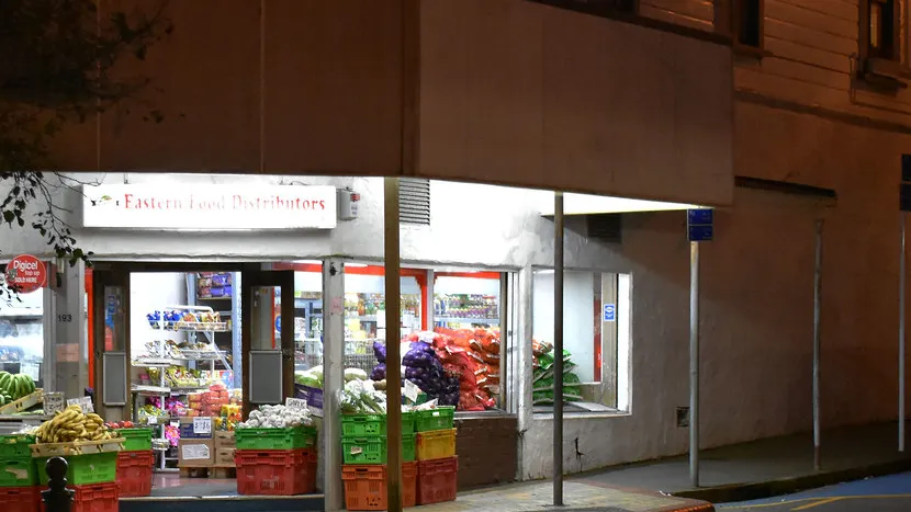 A small grocery store lit up at night on an empty street.